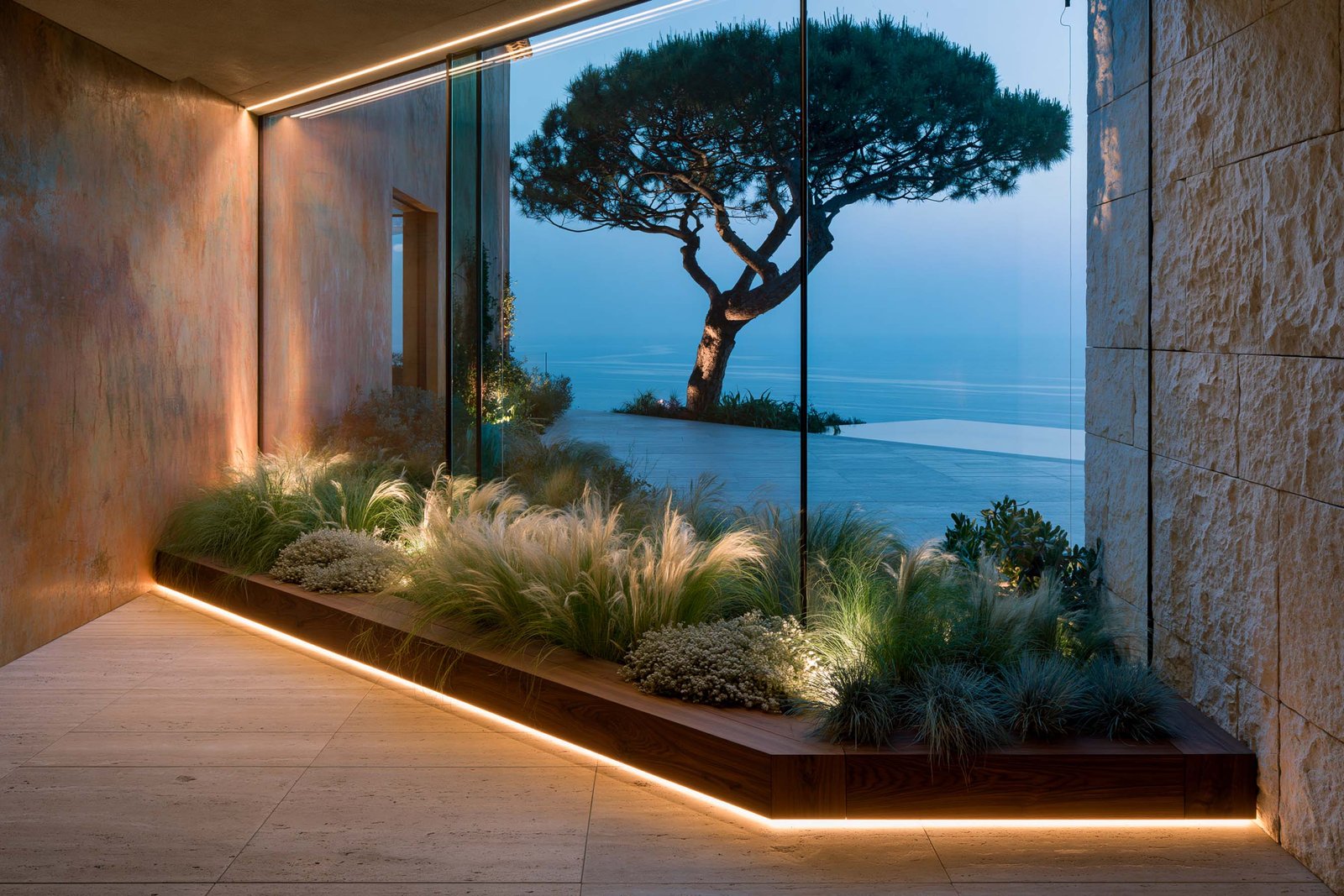 Continuité intérieur-extérieur — loggia vitrée d’une villa à Èze au crépuscule, vue panoramique Méditerranée, intérieur en stucco lustro ocre patiné et mur en pierre calcaire claire brute, planter Lignum™ Block en noyer fumé portant Stipa tenuissima, Helichrysum italicum et Festuca glauca, LED 2700K cachée linéaire au sol, Paracelsus Gardens™