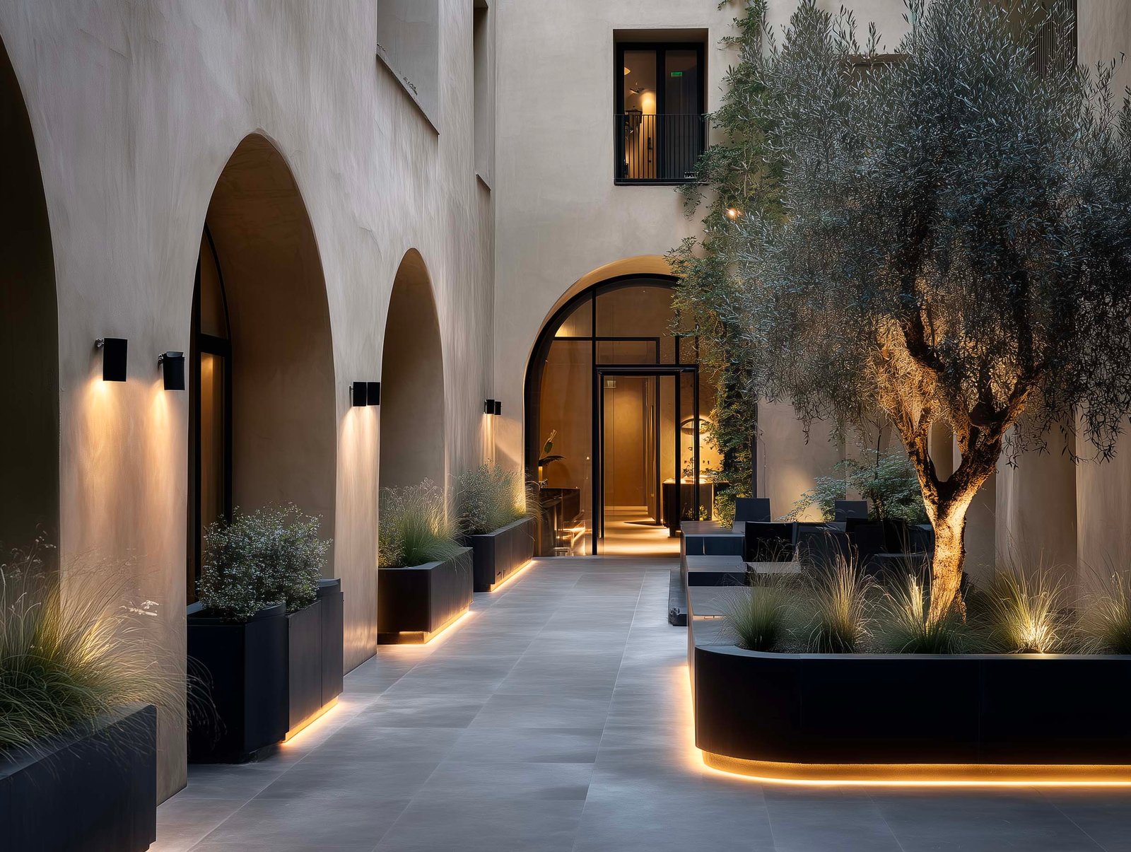 Cortile di hotel con architettura botanica — archi, jardi­nières con LED integrata e olivier centenario, passaggio verso la reception
